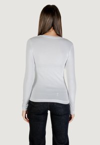 Camisa blanca de manga larga fabricada en una tela suave, con un escote redondeado y una silueta ajustada, combinada con jeans de mezclilla oscura.