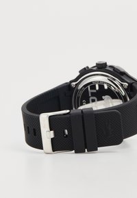Black rubber watch strap with textured surface, silver buckle, and circular watch face displaying a black background and white indices.