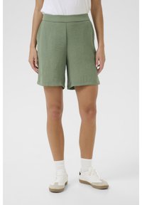 Gröna, texturerade shorts med bred midjeresår, knälång passform och sidofickor. Kombinerat med vita sneakers och ribbade strumpor.