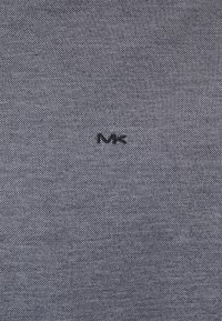 Tissu gris texturé avec un motif subtil et un logo "MK" brodé en noir positionné au centre près du coin inférieur droit.