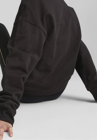 Felpa nera con finitura testurizzata, collo rotondo, spalle scese e polsini a costine. Indossata con leggings sportivi neri.
