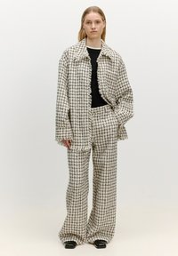 Geruite blazer en broekset in crème en zwart. Gelaagd stof met rafelige randen. Strakke zwarte top eronder. Brede pijpen.