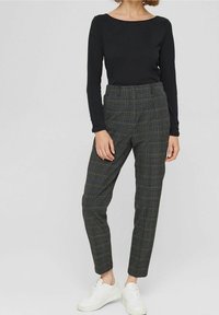 Zwarte top met lange mouwen gecombineerd met grijze geruite broek. De broek heeft een slanke pasvorm en wordt geaccentueerd met witte sneakers.