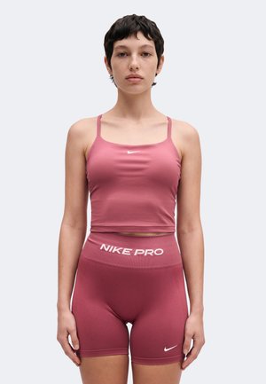 Persoon staat naar voren gericht, draagt roze Nike Pro sportshorts en bijpassende crop top met dunne bandjes en kleine Nike-logo's.