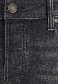 Černá džínová látka s lehkým leskem, viditelným prošíváním, kovovým knoflíkem s logem a hladkou texturou.