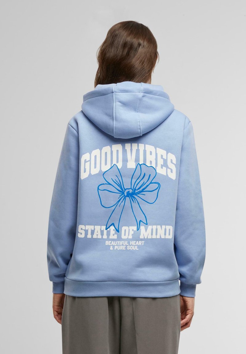 Lyseblå hettegenser med snorhette. Har hvit trykt tekst "GOOD VIBES" og "STATE OF MIND" samt en blå sløytegrafikk.