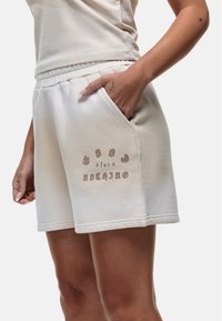 Shorts di cotone beige chiaro con cintura elastica, tasche laterali e una stampa sul davanti con la scritta "GOOD for NOTHING".