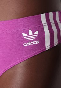 Maillot de bain de sport rose au design ajusté, avec des rayures verticales blanches et un logo Adidas blanc sur la ceinture. Texture lisse.