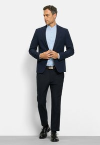 Marineblazer über einem hellblau gestreiften Hemd, kombiniert mit dunklen Hosen und schwarzen Dressschuhen. Verfügt über einen knopfbedienten Frontbereich und ein elegantes Design.