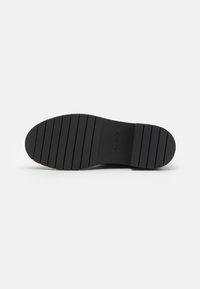 Semelle en caoutchouc noir avec des rainures horizontales pour une meilleure traction. Présente la marque "ALDO" sur le côté. Texture lisse et forme arrondie.