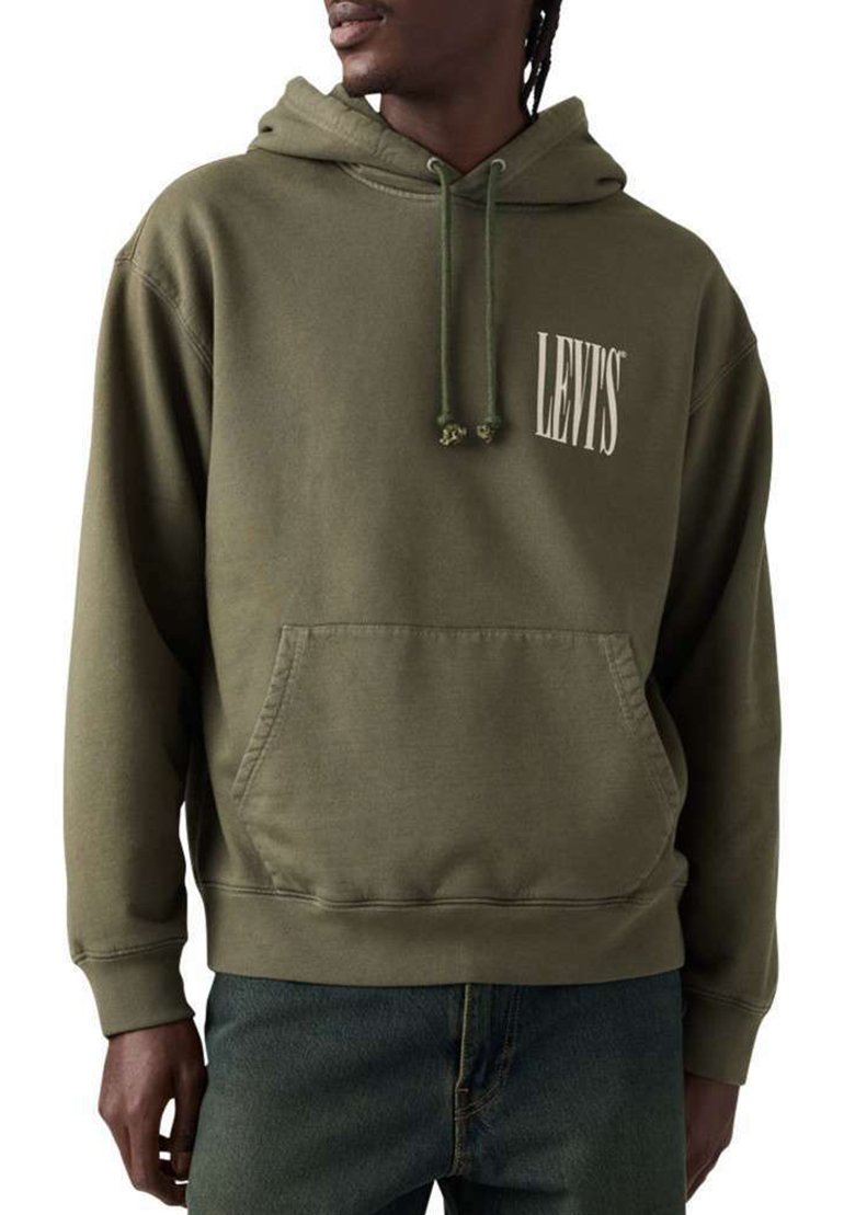 Hombre con sudadera Levi's color verde oliva con bolsillo frontal y capucha con cordón, combinado con vaqueros azules, mirando hacia la izquierda.