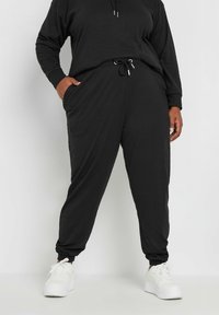 Svart ribbad loungeklädsel med hoodie och joggerbyxor. Har dragsko i midjan och sidofickor. Stylat med vita sneakers.