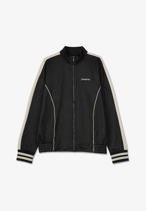 Mustas kapuutsiga jakki, millel on kõrge krae; õlgadel kreemjad triibud ja elastsed mansetid, rinna peal diskreetne logo.