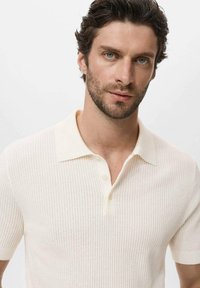 Polo shirt light beige a maniche corte con un motivo a coste testurizzato e un colletto crema morbido, dotato di due bottoni sul collo.