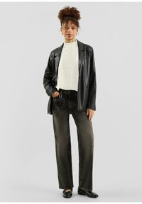 Zwarte leren blazer, witte geribde trui, donkergrijze jeans met wijde pijpen en een met studs versierde accessoire. Zwarte platte schoenen, minimalistische accessoires.