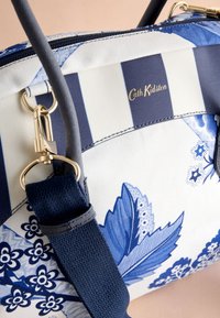 Blå och vit mönstrad väska med blomsterdesign, randiga sektioner, guldfärgade detaljer, stadiga remmar och texturerad yta. Märkeslogga synlig.