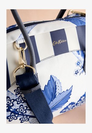 Modra in bela torba s cvetličnimi vzorci, črtastimi deli, zlatim kovinskim okrasjem, trdnimi trakovi in teksturirano površino. Vidna je znamčna oznaka.