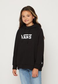 Felpa nera con cappuccio e logo bianco "VANS", caratterizzata da una vestibilità comoda, polsini a coste e spacchi laterali, abbinata a jeans blu chiaro.