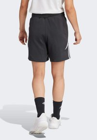 Pantaloni sportivi neri in tessuto, con una striscia laterale bianca, vita elastica e vestibilità comoda. Indossati con calzini neri a coste.