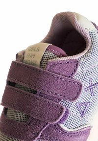 Scarpa sportiva viola e bianca con tomaia in mesh, sovrapposizioni in suede e fasce in Velcro. Il testo sulla linguetta recita "LE RAGAZZE CORSANO PIÙ VELOCE".