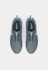 Ζεύγος γκρι αθλητικά παπούτσια Nike με λευκά λογότυπα Swoosh, λευκές μεσαίες σόλες και ανακλαστικές θηλιές έλξης, φαίνεται από πάνω σε λευκό φόντο.