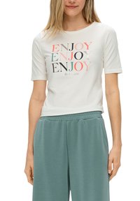 Witte T-shirt met korte mouwen waarop het woord "ENJOY" in meerdere kleuren en lettertypes staat, gecombineerd met groene joggingsbroek met elastische taille.