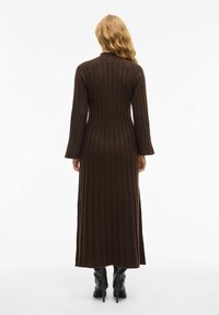 Robe en tricot côtelé brun à manches longues, col montant et silhouette ajustée s'étendant jusqu'au mollet, associée à des bottes à talons noires.