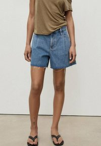 Jeansshorts i medelblått med sicksackkant, hög midja och två framfickor; i kombination med en figurnära topp i olivgrönt.