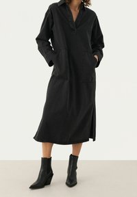 Czarna sukienka dżinsowa z kołnierzykiem, bocznymi kieszeniami i prostym krojem. Posiada długie rękawy oraz boczny rozcięcie dla swobody ruchów.