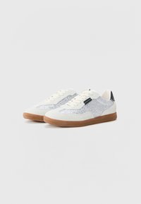 Sneakers with a white suede upper, silver sparkly accents, and a brown rubber sole. Features flat laces and a black heel detail.