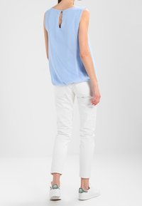 Top sin mangas de color azul claro con un diseño de abertura en la espalda, combinado con pantalones ajustados blancos y zapatillas blancas con detalles verdes.
