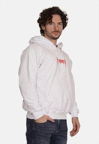 Felpa bianca con tasca frontale a marsupio, cappuccio con coulisse e testo grafico rosso sul petto. Presenta polsini e orlo a coste.