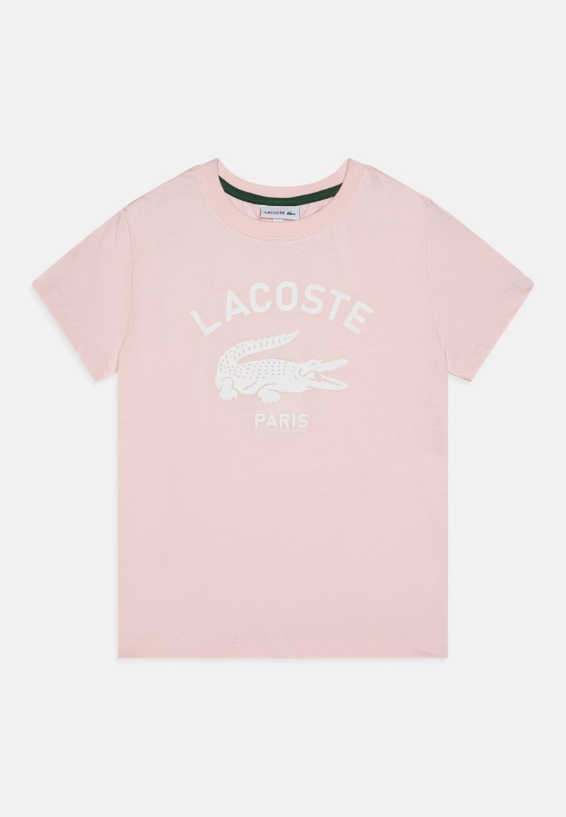 Camiseta de algodón rosa claro con un logo blanco de Lacoste y un gráfico de cocodrilo. Manga corta y cuello redondo con una etiqueta interior verde.