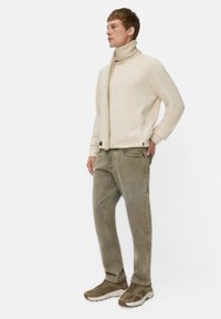 Beige sweater med høj hals, parret med olivengrønne løse jeans. Modellen bærer et matchende beige ribbet tørklæde og brune sneakers.