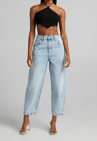 Black ribbed halter crop top with a scalloped hem paired with high-waisted light blue wide-leg jeans. Clear block-heel mules are worn.