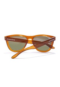 Pomarańczowe, przezroczyste okulary przeciwsłoneczne z ciemnozielonymi soczewkami i eleganckim designem. Ramiona zdobi biały logo "HAWKERS".