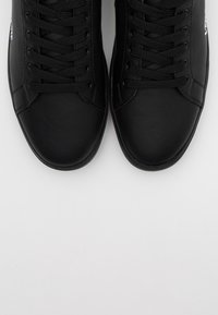 Svarta läderskor har en slät yta, rund tå och platt snörning med en tonad plös och minimalistisk design.