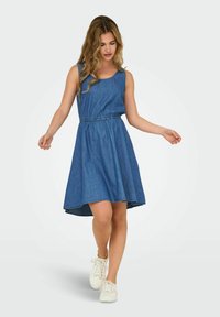 Denim bešvarkis su apvalia iškirpte, elastinga juosmens linija ir platėjančia sijonu. Audinys yra vidutinio mėlynumo atspalvio su lygiu paviršiumi.