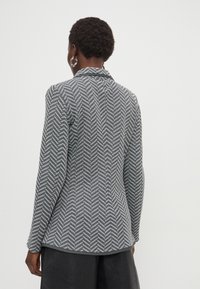 Americana gris de pata de gallo con un corte entallado, mangas largas y cuello de muesca. Tejido texturizado con una abertura trasera y líneas limpias.