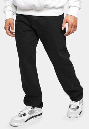 Schwarze Jeans aus Denim mit geradem Schnitt, ausgestattet mit Hüfttaschen und dezenten Nähten, kombiniert mit weißen und schwarzen Sportschuhen.