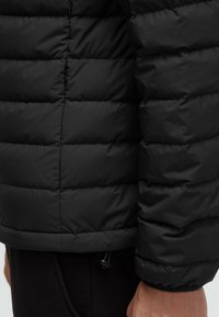 Black puffer jacket with quilted design, featuring a textured surface and an adjustable drawstring at the hem for a customized fit.