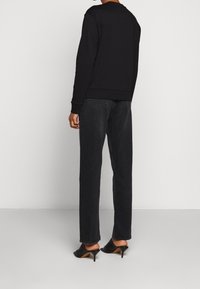 Schwarzer Sweatshirt mit Rundhalsausschnitt und gerippten Bündchen, kombiniert mit dunkelblauen Denim-Jeans und schwarzen offenen Sandalen, von hinten gesehen.