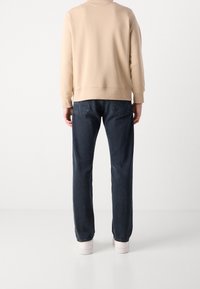 Sudadera beige con puños acanalados, combinada con jeans de pierna recta en azul oscuro. El conjunto se completa con zapatillas blancas.