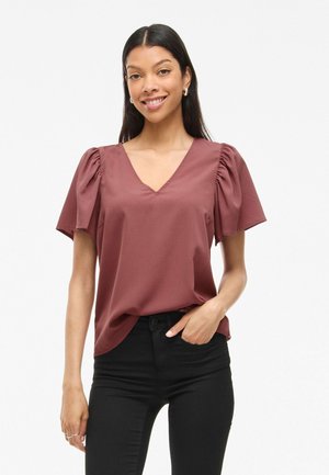 Blouse courte à manches courtes bordeaux avec un col en V, présentant des manches bouffantes et une texture lisse. Associée à un pantalon ajusté noir.
