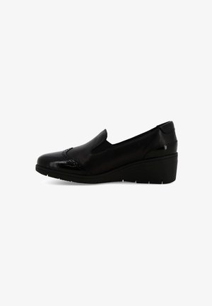Scarpa slip-on in pelle nera con dettagli brogue e una spessa suola a cuneo, vista di lato su uno sfondo bianco.