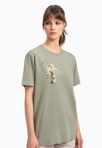 T-shirt in cotone verde oliva con maniche corte, caratterizzato da un'illustrazione grafica sul davanti e una vestibilità ampia e rilassata.
