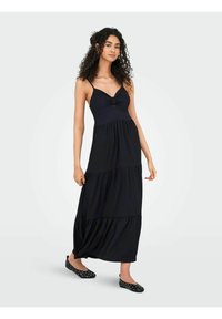 Robe maxi noire avec un corsage ajusté, un détail central noué et une jupe à volants. Fabriquée en tissu doux, elle présente de fines bretelles spaghetti.