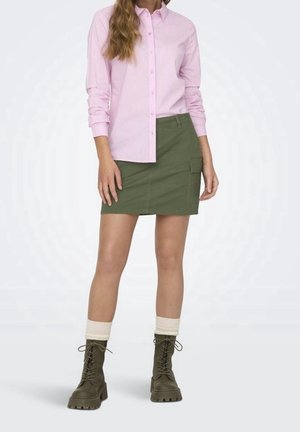 Vaaleanpunainen raidallinen nappipusero, vihreät cargo-tyyliset hameet sivutaskuilla ja vihreät nauhakitkaiset saappaat tekstuuripohjalla ja valkoisilla hihansuilla.