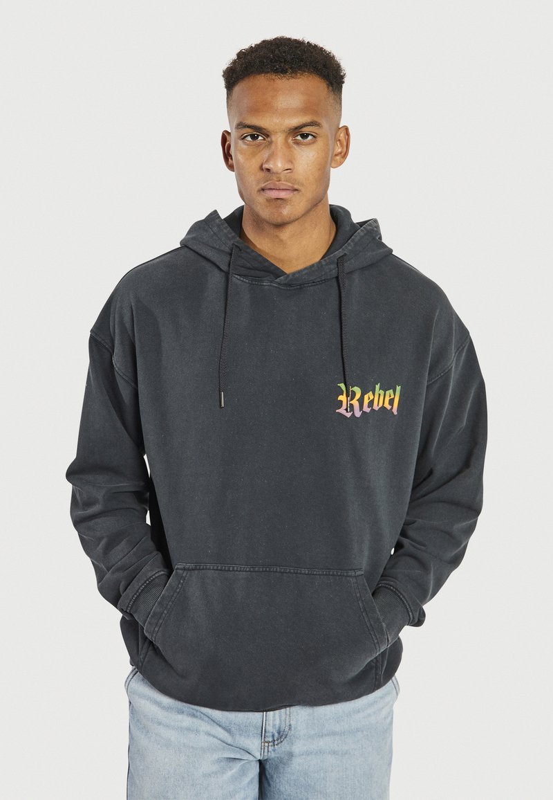 Czarny, oversize'owy hoodie wykonany z bawełny, posiadający przednią kieszeń, sznurki oraz kolorowy napis "Rebel" na lewej piersi.