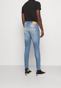 Vaqueros de mezclilla azul claro con un corte ajustado, con un parche de cuero marrón en la parte de atrás y complementados con zapatillas altas negras.